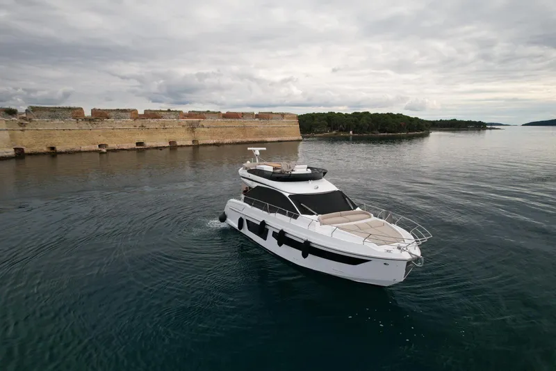  Yacht Photos Pics 2024 Azimut Fly 53 yacht cruising near a historic stone wall on a cloudy day.
