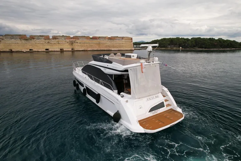  Yacht Photos Pics 2024 Azimut Fly 53 yacht cruising near a historic stone wall and lush greenery.