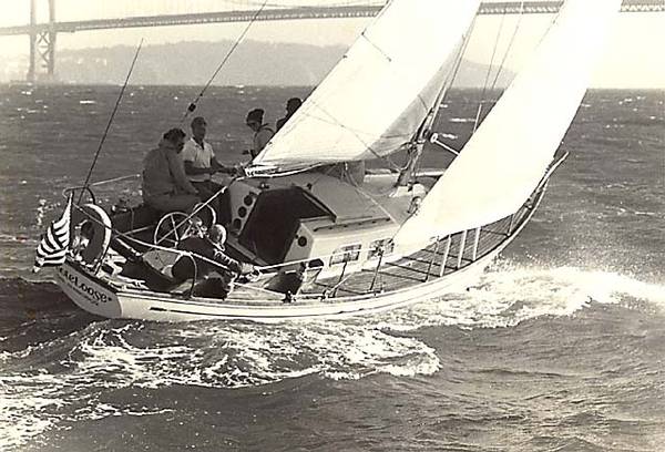 1965 Pearson Vanguard sailboat navigating choppy waters with crew, bridge in background.