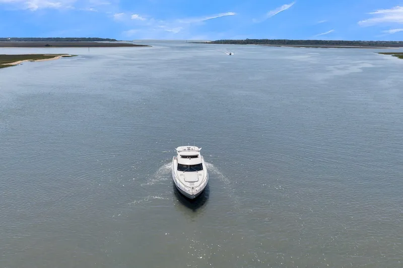  Yacht Photos Pics 2020 Riviera 4800 Sport Yacht cruising on a wide, calm river under a clear blue sky.