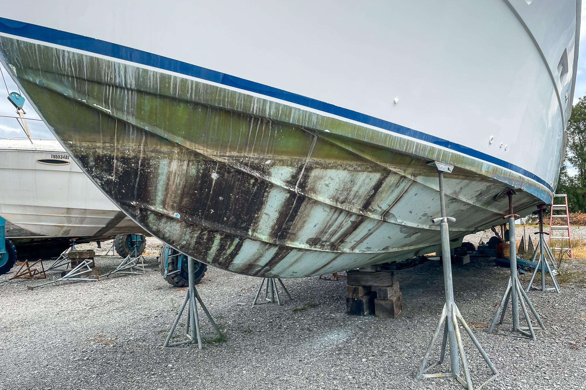 1978 Bertram 46 Convertible boat on stands, showing hull with algae and rust.