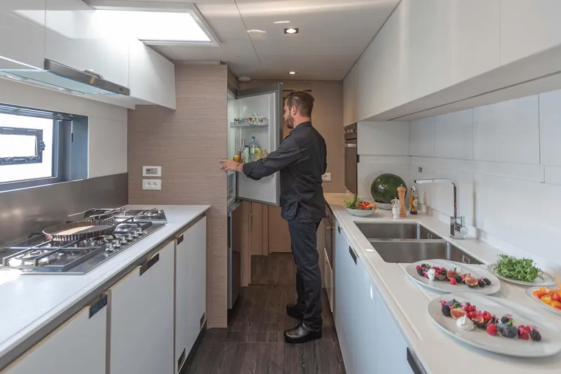  Yacht Photos Pics Modern kitchen interior on 2026 Fountaine Pajot Samana 59 yacht with chef preparing food.