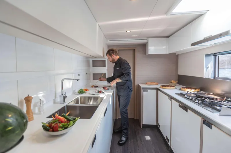  Yacht Photos Pics Modern kitchen interior on 2026 Fountaine Pajot Samana 59 yacht, featuring a chef preparing food.