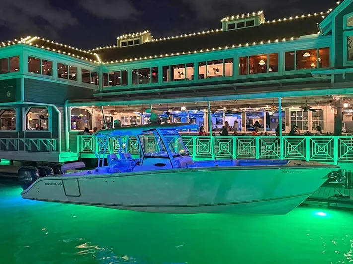  Yacht Photos Pics 2018 Cobia 344 Center Console boat illuminated at night near a waterfront restaurant.