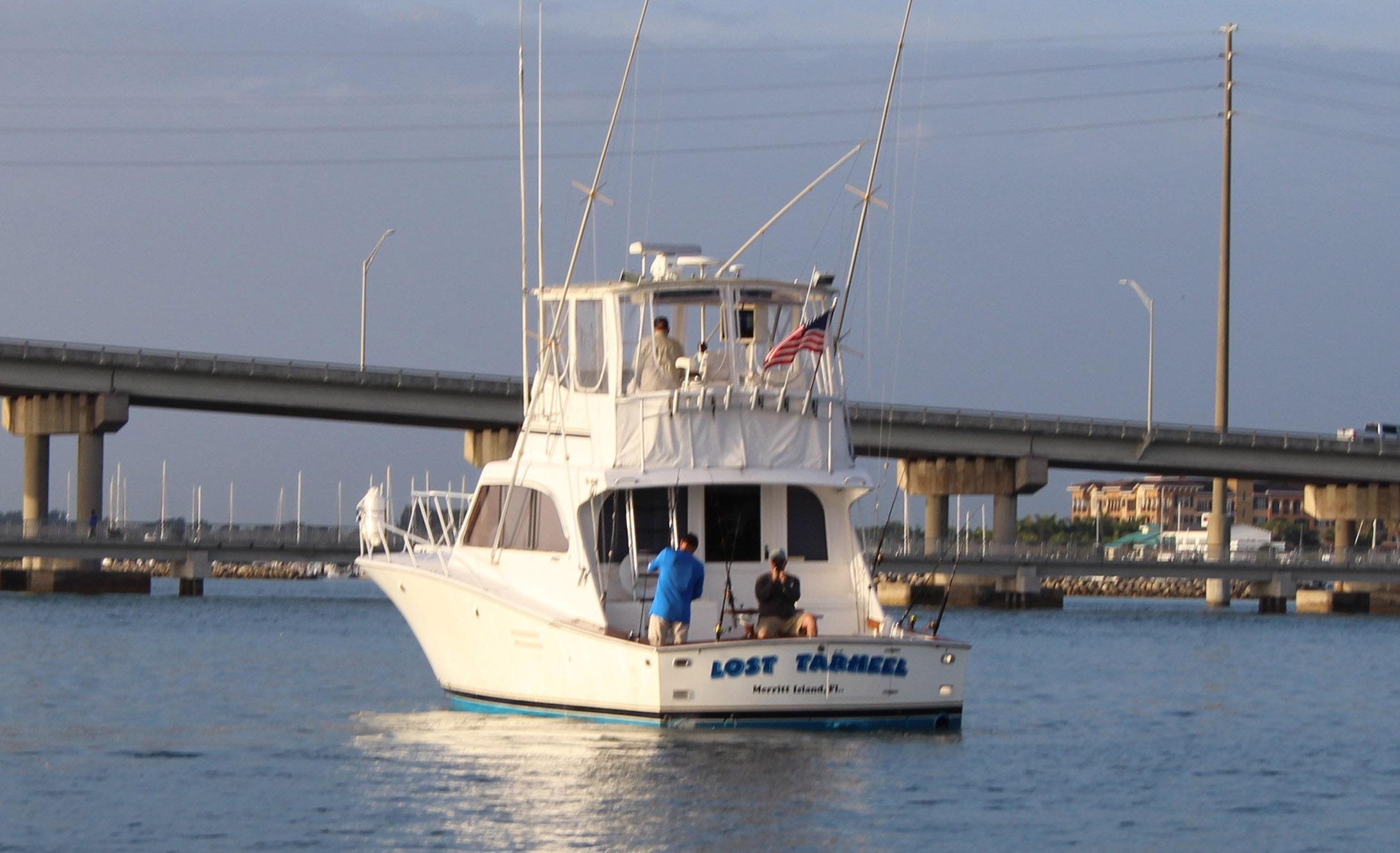 1990 Post 44 Sport Fisherman boat on water near a bridge, with people on deck.