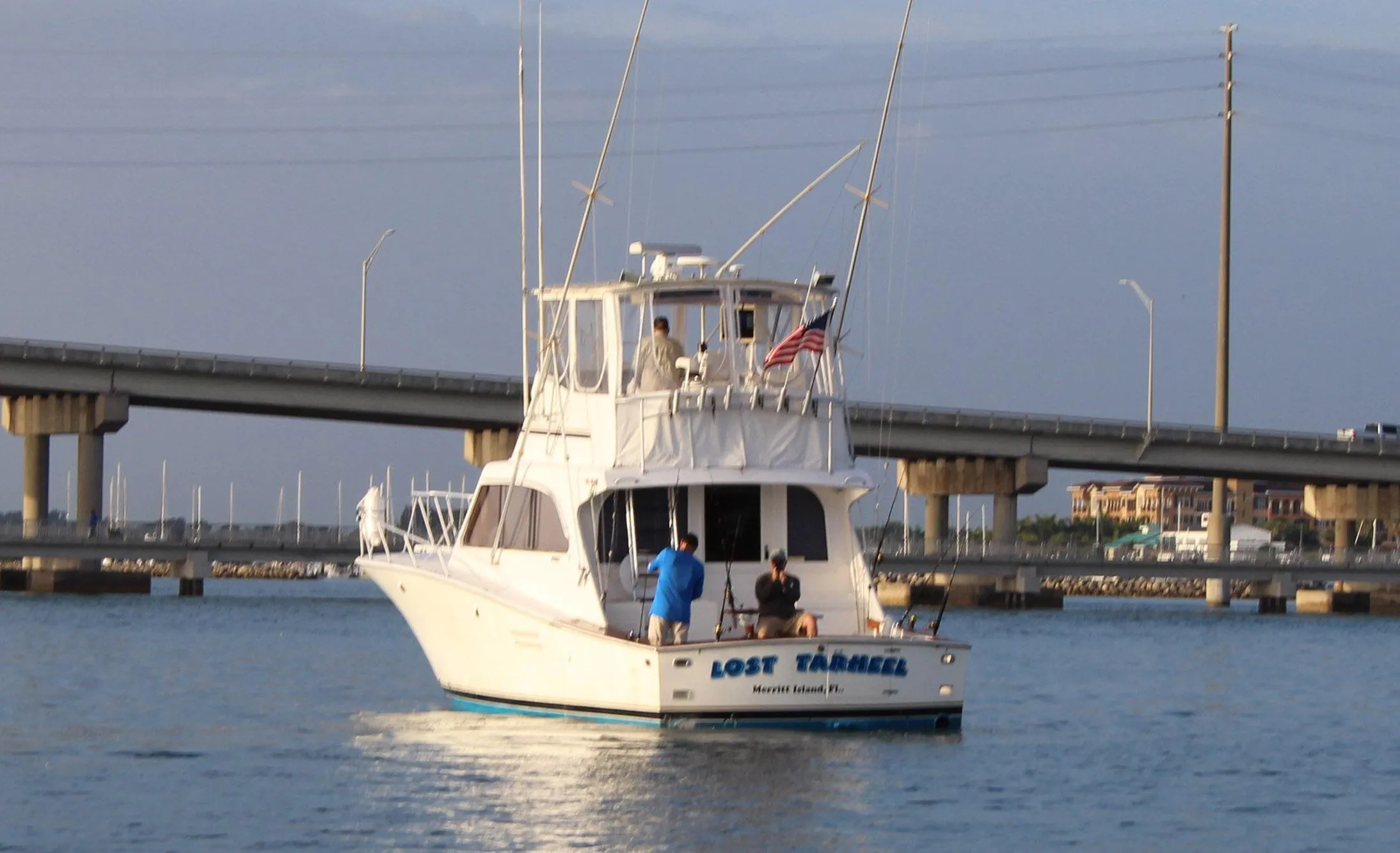 1990 Post 44 Sport Fisherman boat on water near a bridge, with people on deck.