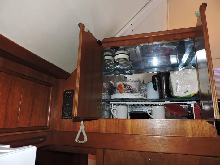  Yacht Photos Pics Open wooden cabinet in 1990 Post 44 Sport Fisherman yacht kitchen, displaying dishes and kitchenware.