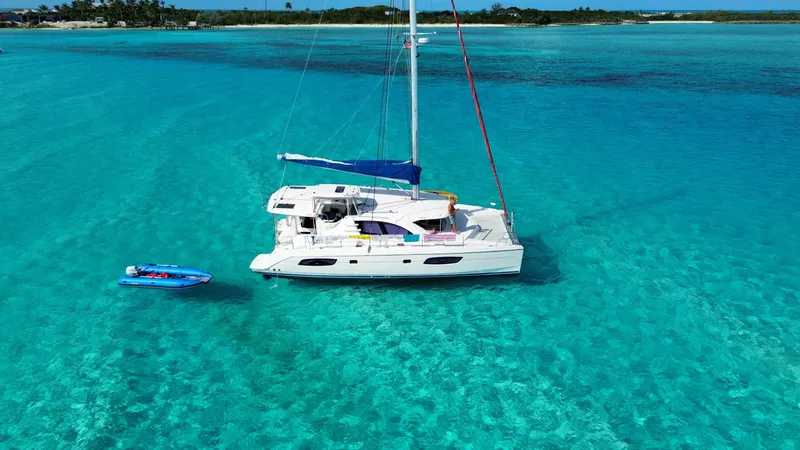 Merry Mac Yacht Photos Pics Catamaran Leopard 44 sailing in clear turquoise waters, 2013 model, with a small blue dinghy nearby.