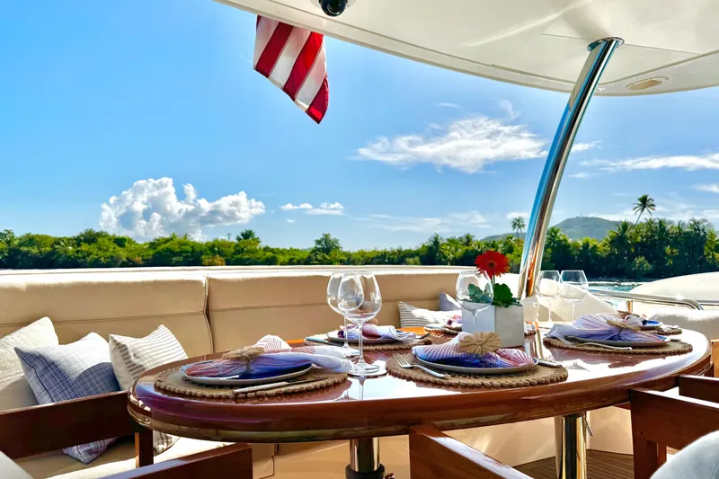 Tortuga Yacht Photos Pics Luxurious Horizon E88 yacht dining area with elegant table setting, tropical backdrop, and American flag.
