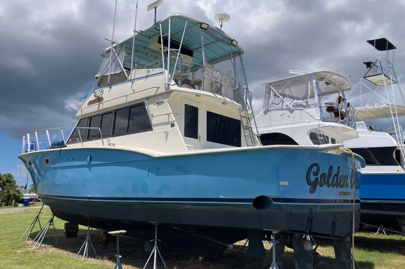 Golden Olive Yacht Photos Pics 1985 Hatteras Sportfish boat on stands, blue hull, cloudy sky background.
