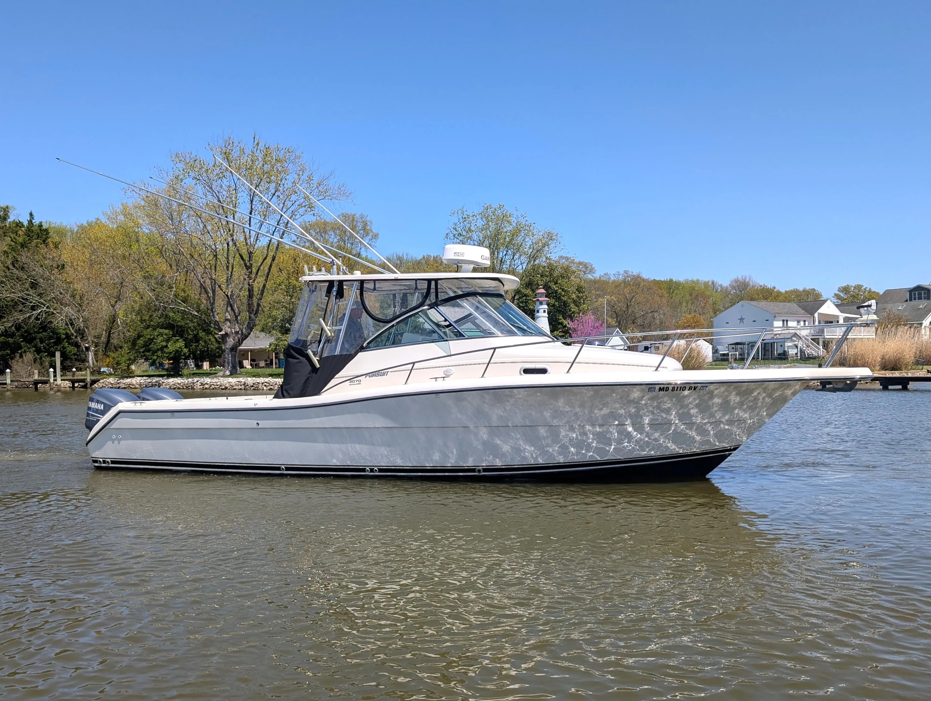 2001 Pursuit 3070 Offshore Center Console boat on calm water, surrounded by trees and houses.