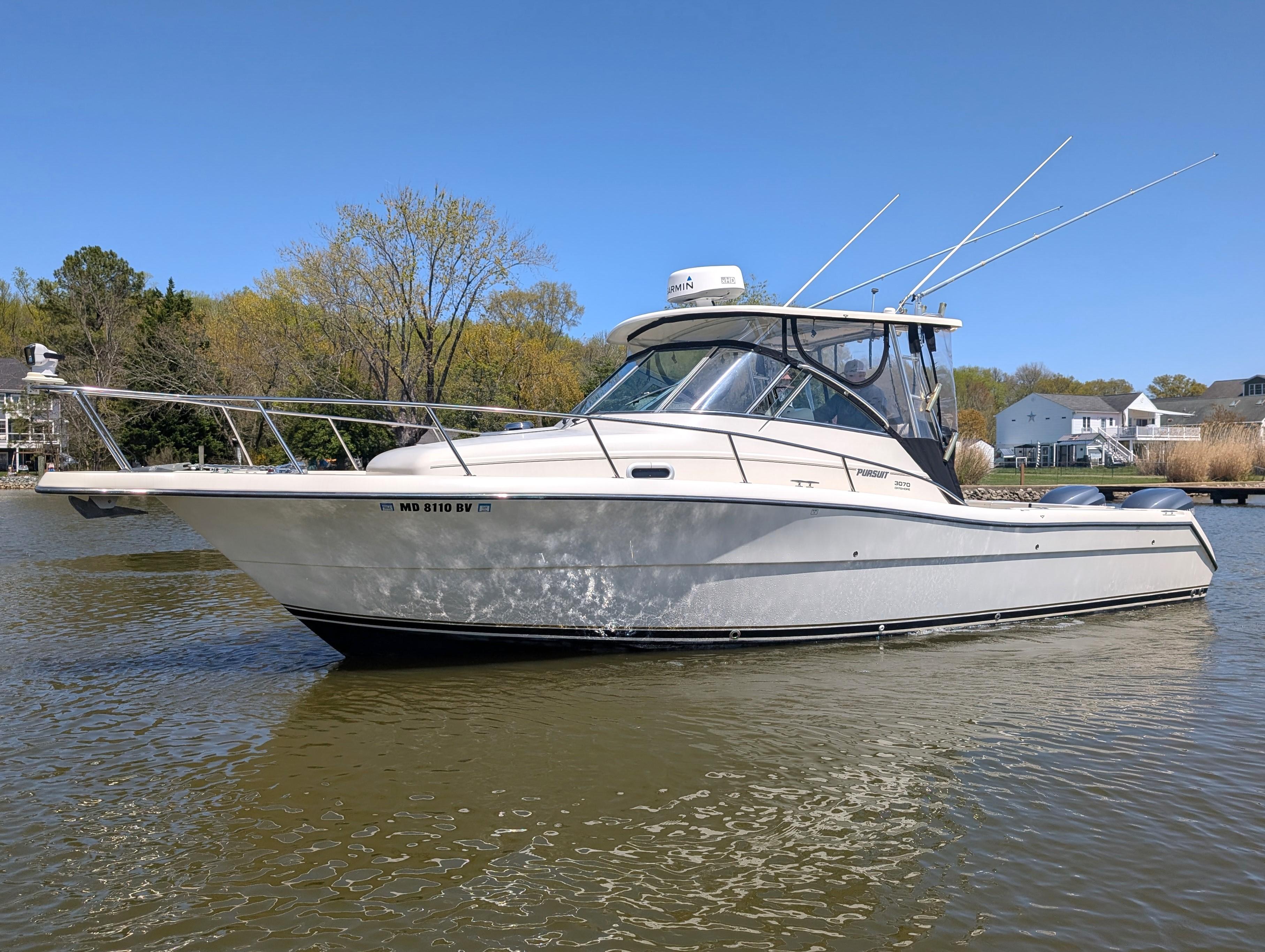 2001 Pursuit 3070 Offshore Center Console boat on calm water, surrounded by trees and houses.