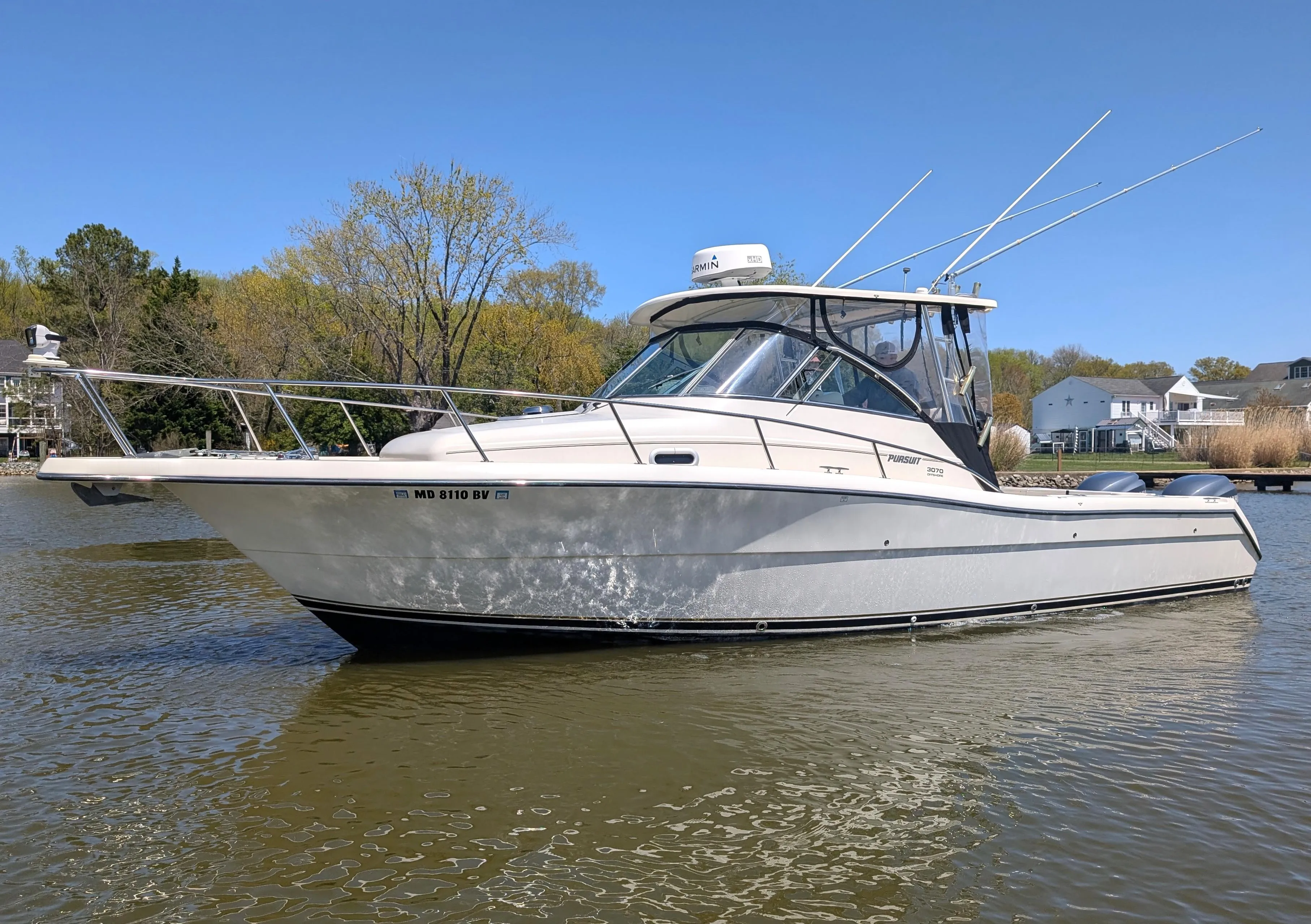 2001 Pursuit 3070 Offshore Center Console boat on calm water, surrounded by trees and houses.