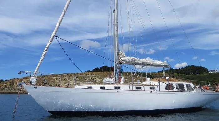 Classic 1968 Raymond Labbé Sloop sailing near rocky coastline under blue sky.