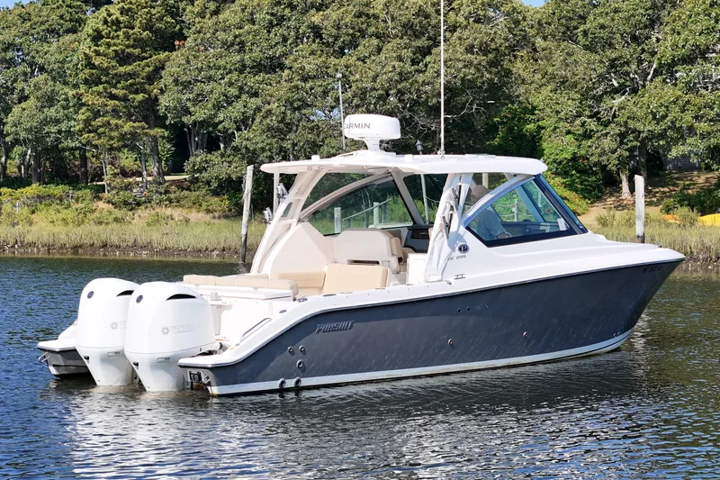 Yacht Photos Pics 2018 Pursuit DC 295 Dual Console boat on calm water, surrounded by lush greenery.