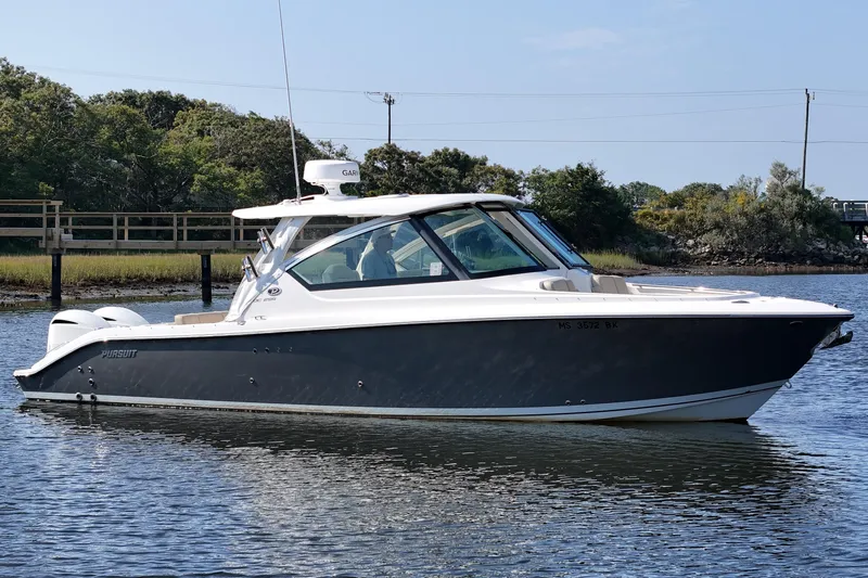  Yacht Photos Pics 2018 Pursuit DC 295 Dual Console boat on calm water, surrounded by lush greenery.