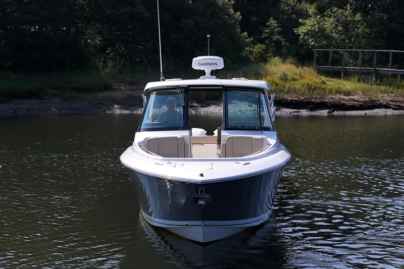  Yacht Photos Pics 2018 Pursuit DC 295 Dual Console boat on calm water, surrounded by greenery.