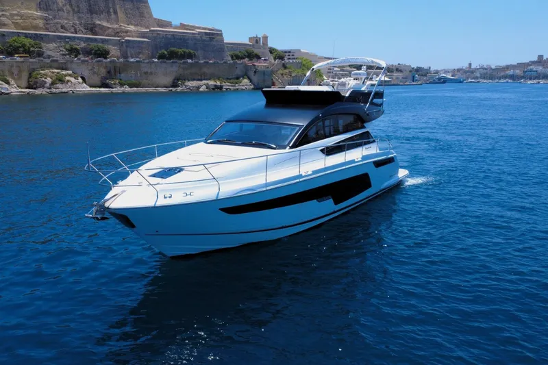 Waypoint Yacht Photos Pics 2024 Fairline Squadron 50 yacht cruising on clear blue waters near a rocky coastline.