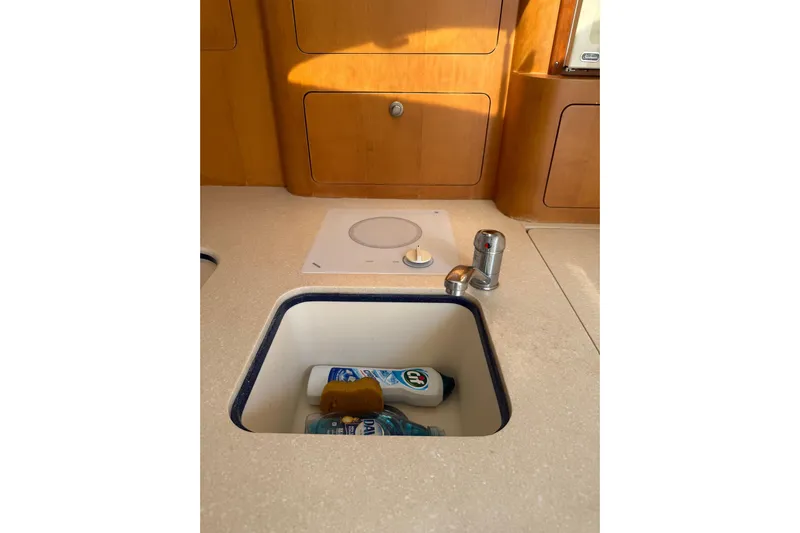 Chapuzon III Yacht Photos Pics 2001 Intrepid 377 Walkaround kitchen sink with cleaning supplies, wooden cabinetry background.