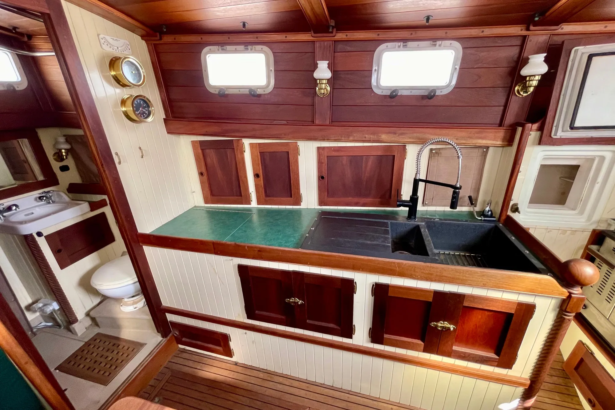 Wooden boat interior with vintage kitchen and bathroom, featuring brass fixtures and porthole windows.