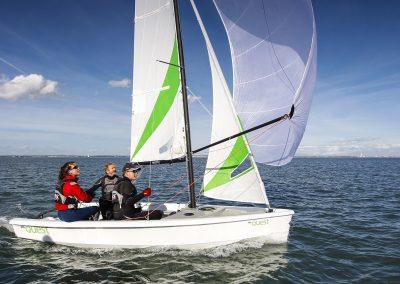 2023 RS Quest sailboat with three people sailing on open water.