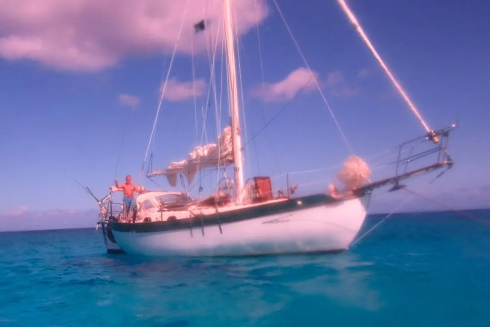 1977 Westsail Cutter sailboat on clear blue ocean under a vibrant sky.