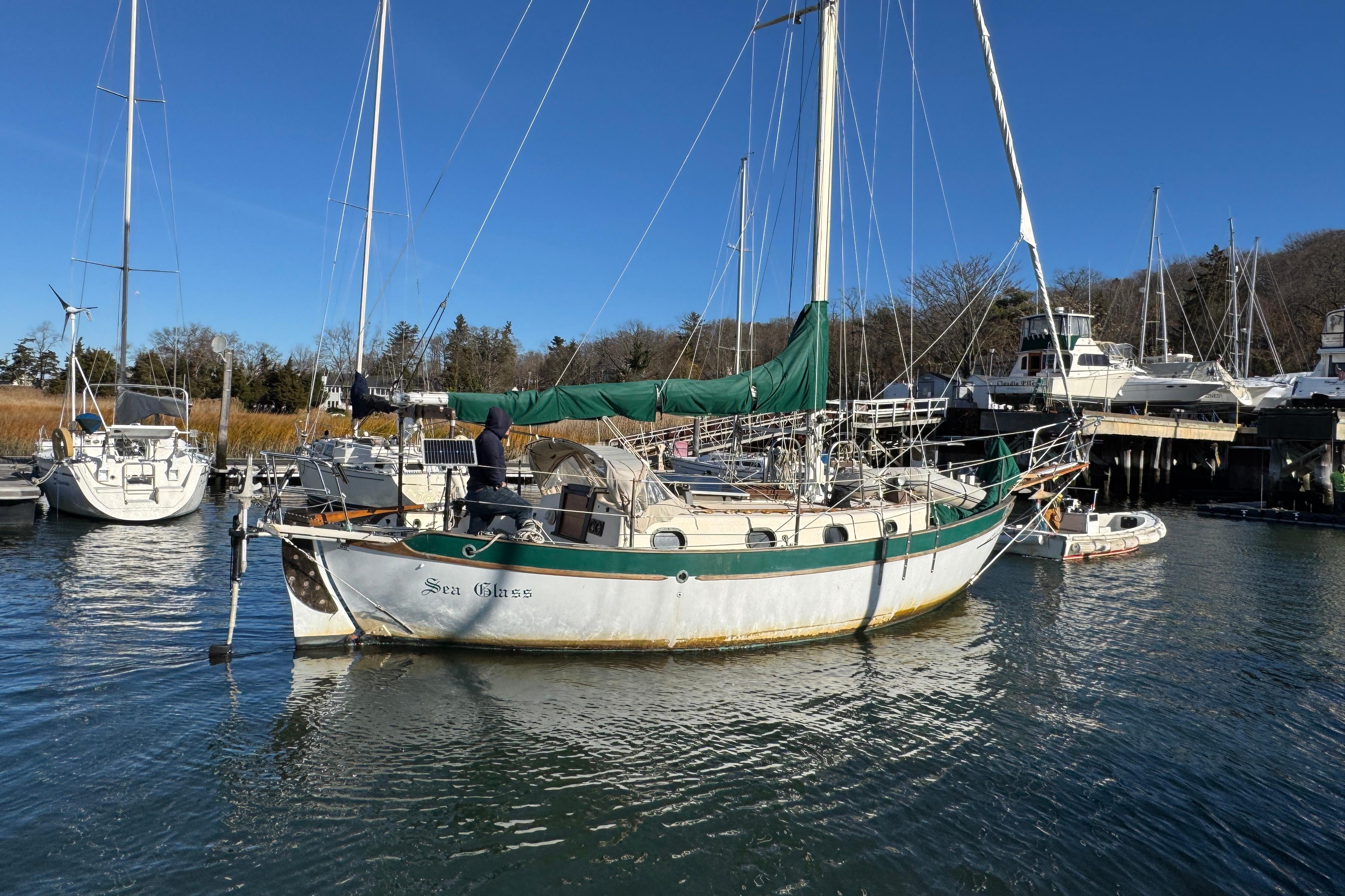 1977 Westsail Cutter sailboat docked in a marina, featuring green sails and a calm water setting.
