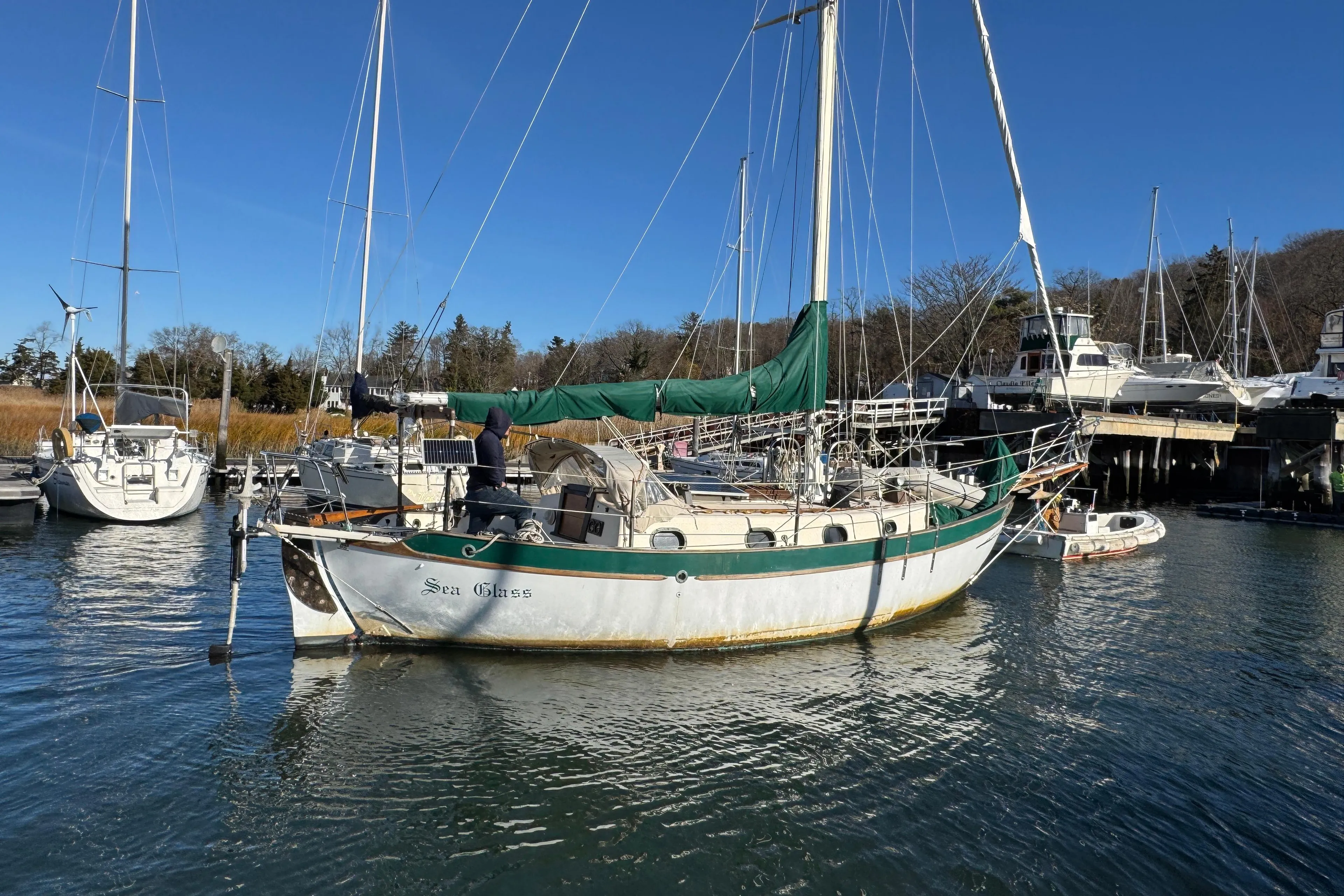 1977 Westsail Cutter sailboat docked in a marina, featuring green sails and a calm water setting.