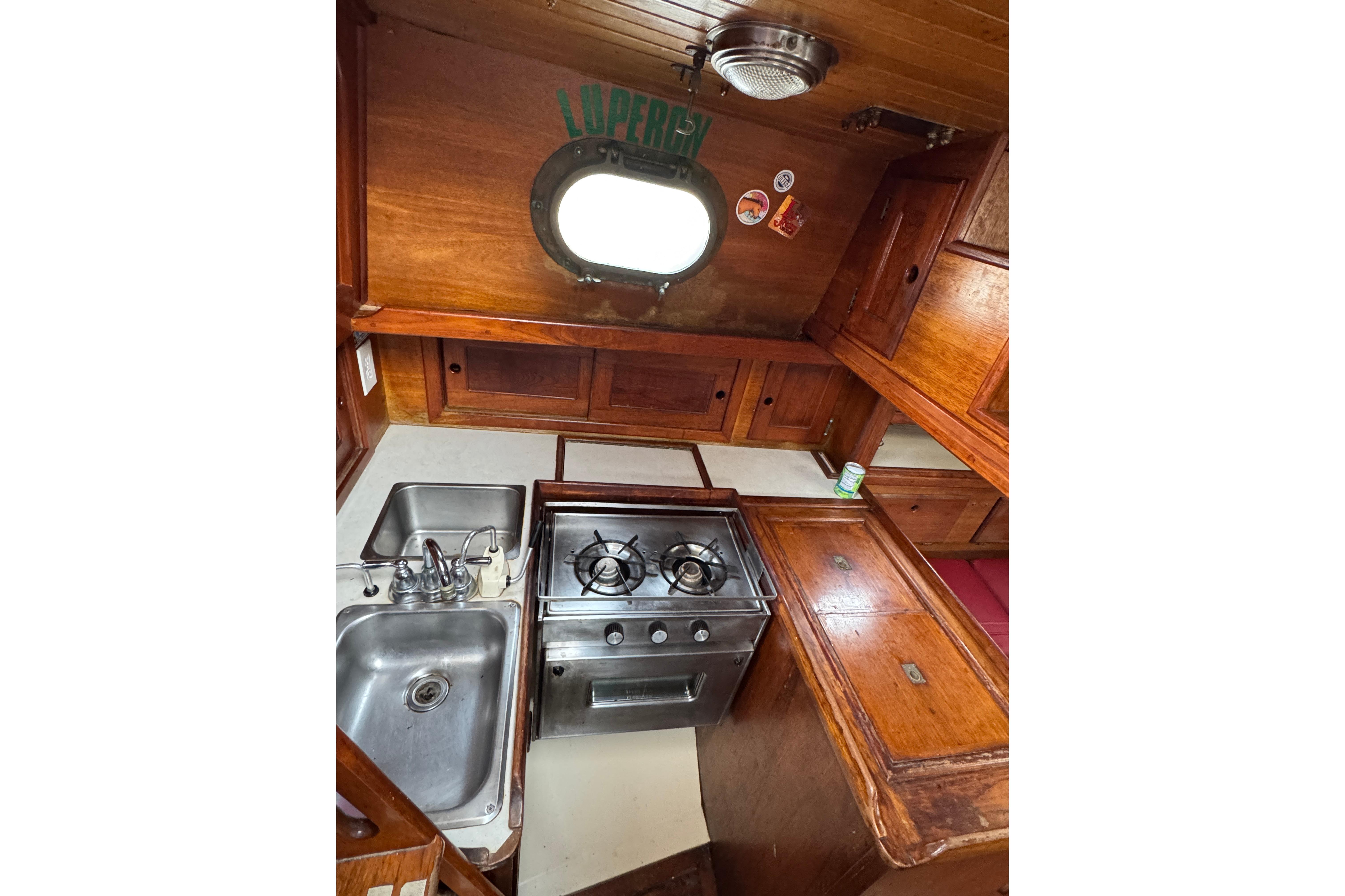 1977 Westsail Cutter galley with wooden cabinetry, stainless steel sink, and stove.
