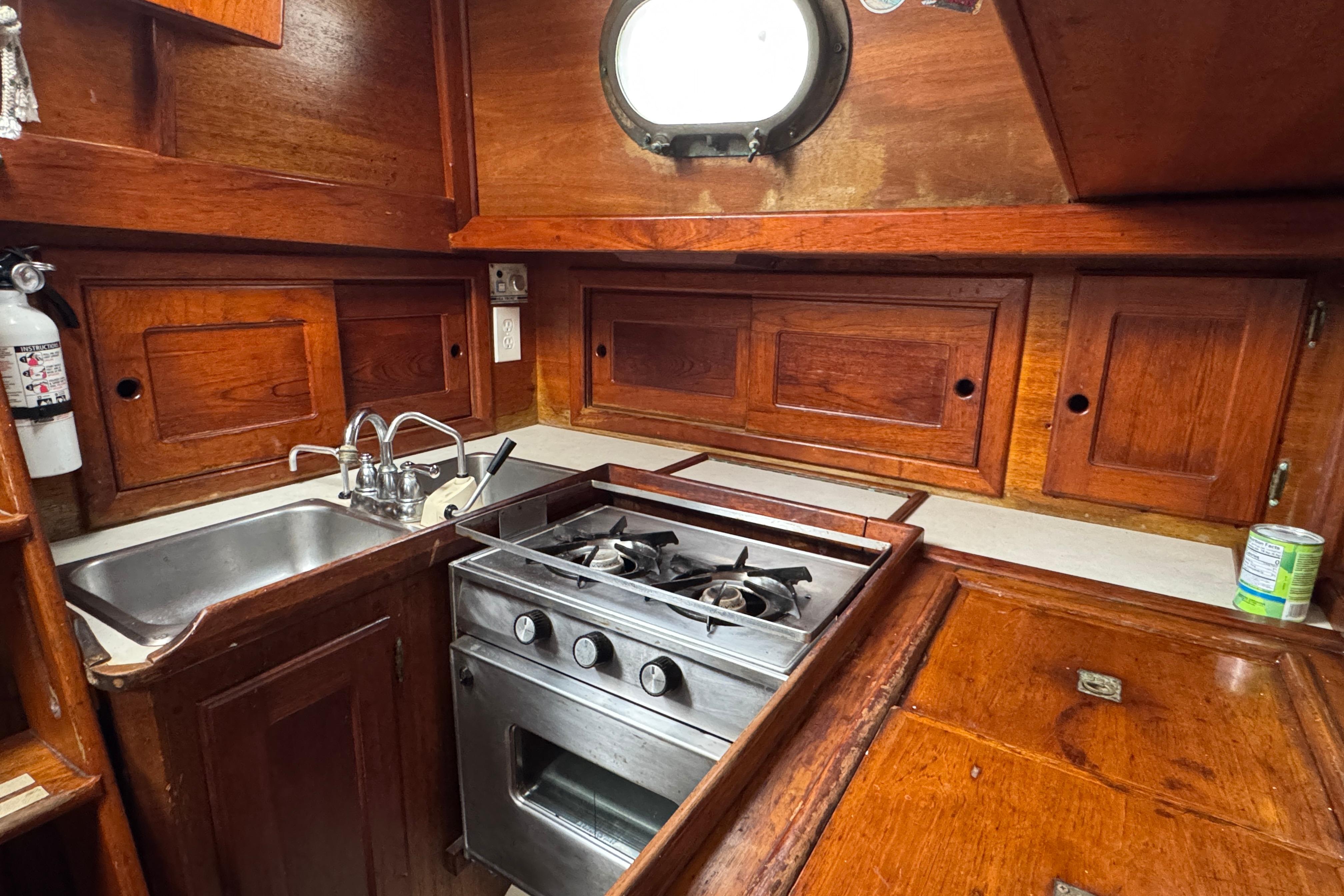 1977 Westsail Cutter kitchen with wooden cabinets, stainless steel stove, and sink.