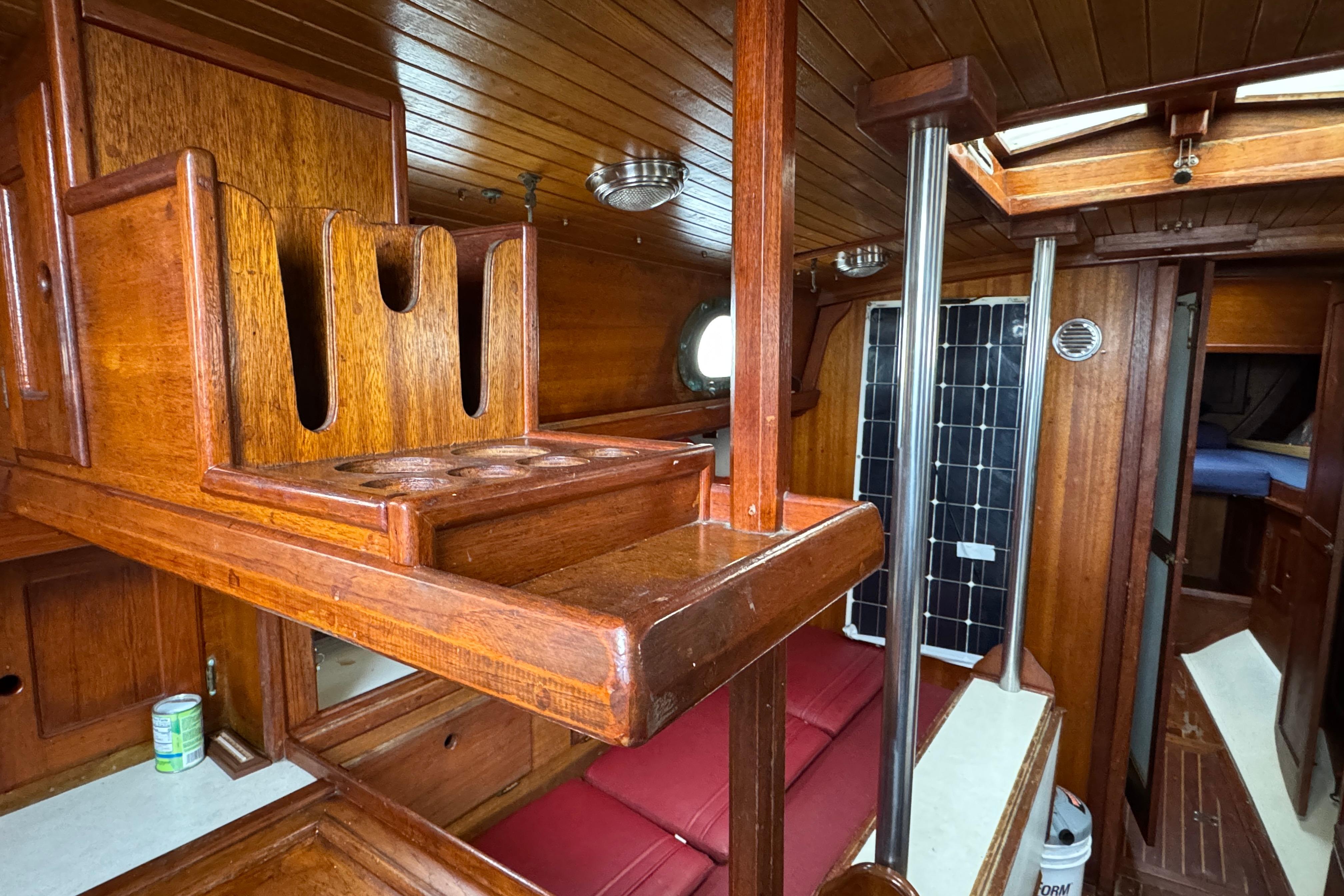 1977 Westsail Cutter interior with wooden cabinetry, red seating, and solar panel.