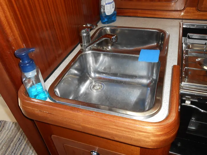 Pilitak Yacht Photos Pics Kitchen sink area in a 2001 Bavaria 37 yacht, featuring wooden cabinetry and cleaning supplies.