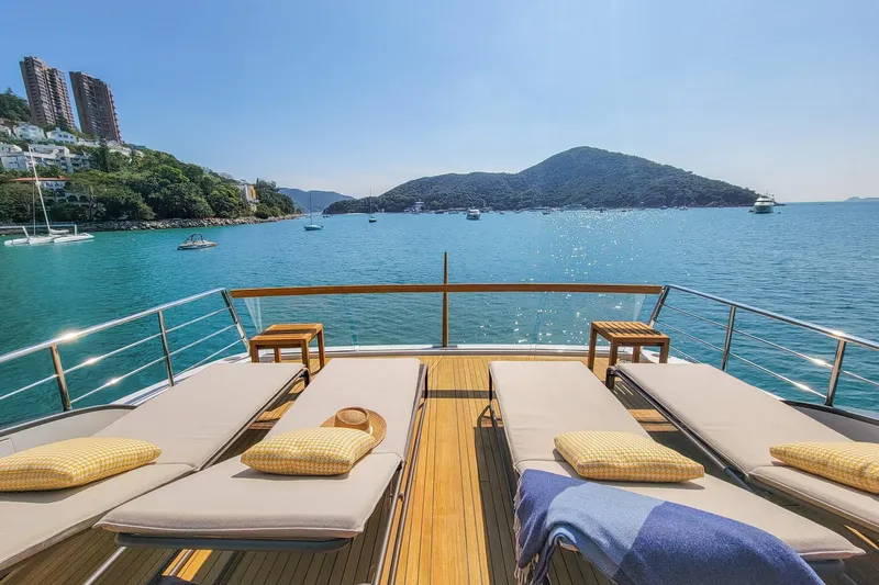  Yacht Photos Pics Luxurious Sanlorenzo SL78 yacht deck with sun loungers, overlooking serene blue waters and distant hills.