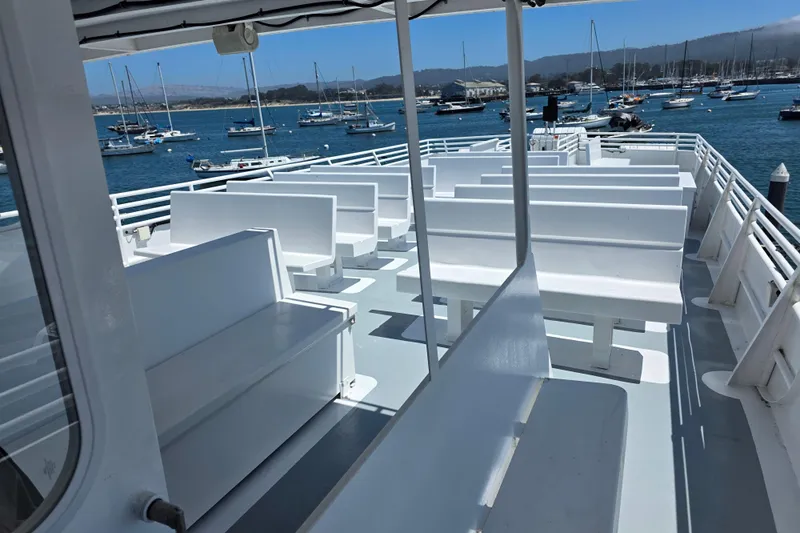 Ocean Thunder Yacht Photos Pics Open deck of 1986 Gulf Craft Passenger boat with white benches, docked in marina.