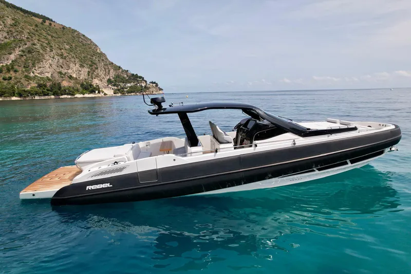Rebel 47 Yacht Photos Pics 2025 SACS Rebel 47 luxury boat on clear blue water near a scenic coastline.