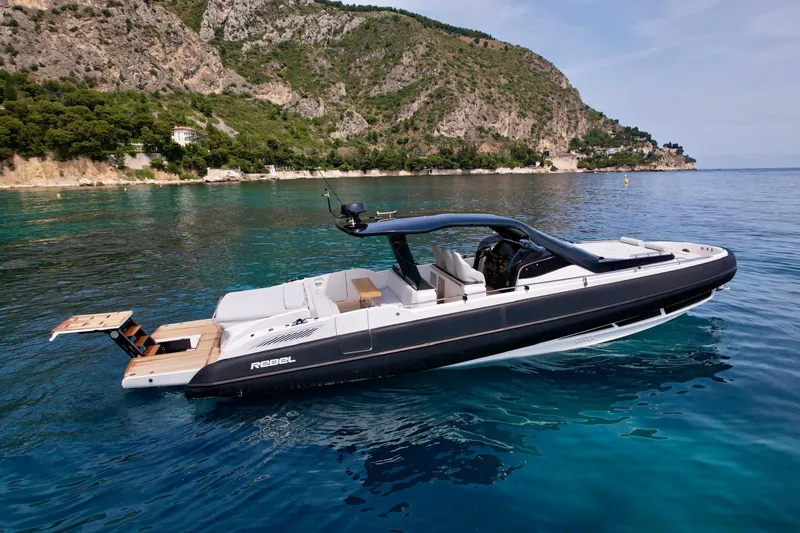 Rebel 47 Yacht Photos Pics 2025 SACS Rebel 47 yacht on clear blue water near rocky coastline.