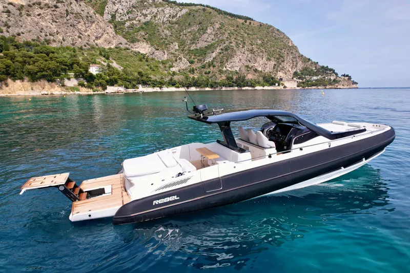 Rebel 47 Yacht Photos Pics 2025 SACS Rebel 47 yacht on clear blue water near rocky coastline.