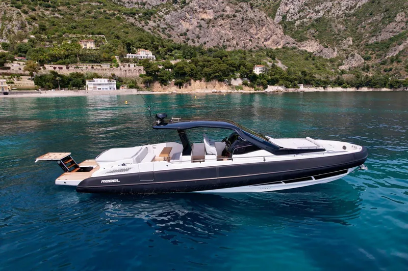 Rebel 47 Yacht Photos Pics 2025 SACS Rebel 47 luxury yacht on clear blue water near a rocky coastline.