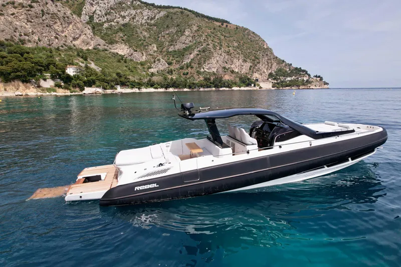 Rebel 47 Yacht Photos Pics 2025 SACS Rebel 47 yacht on clear blue water near rocky coastline.