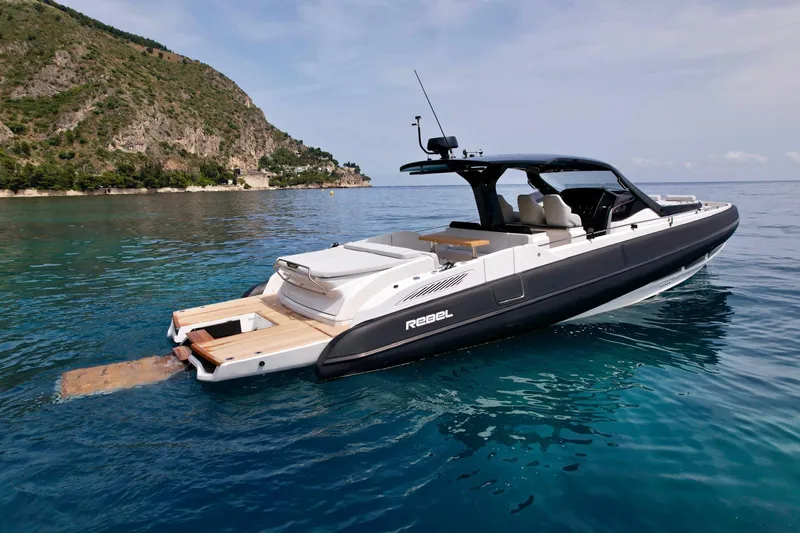 Rebel 47 Yacht Photos Pics 2025 SACS Rebel 47 luxury yacht on clear blue water near a scenic coastline.