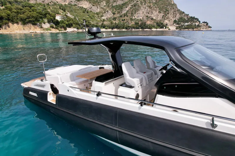 Rebel 47 Yacht Photos Pics 2025 SACS Rebel 47 luxury boat on clear blue water near rocky coastline.