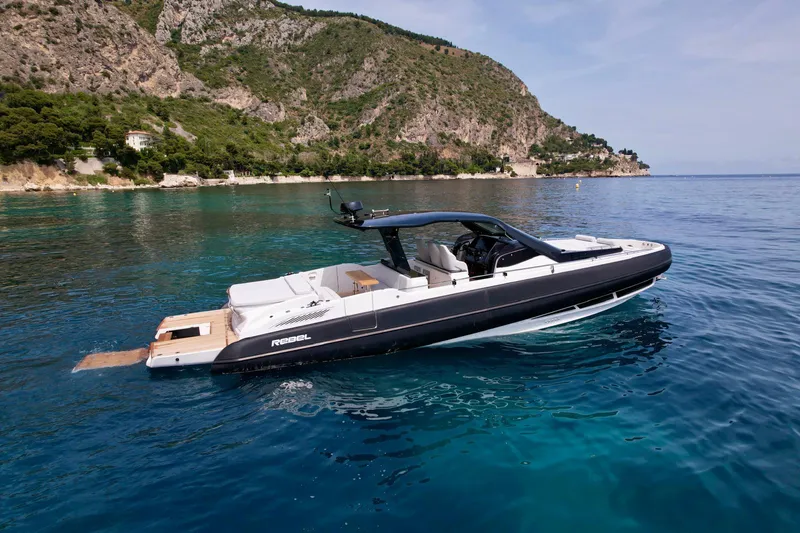 Rebel 47 Yacht Photos Pics 2025 SACS Rebel 47 yacht cruising in clear blue waters near a rocky coastline.