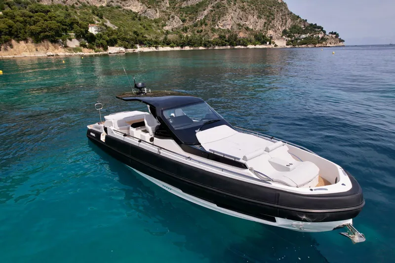 Rebel 47 Yacht Photos Pics 2025 SACS Rebel 47 luxury yacht on clear blue water near a rocky coastline.