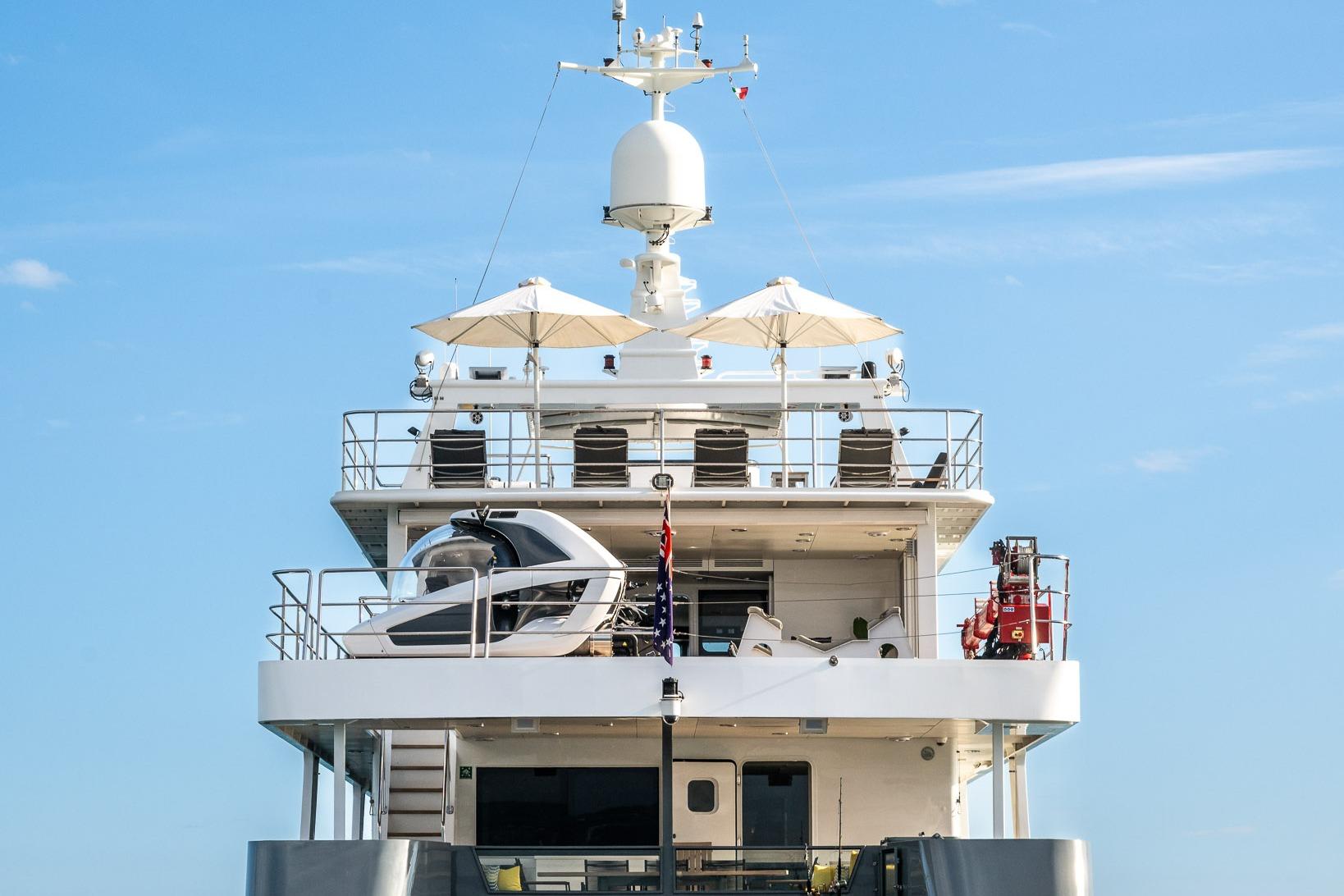 Luxury yacht deck with helicopter, Tenix Defence ICE Explorer, 2005 model, under clear blue sky.