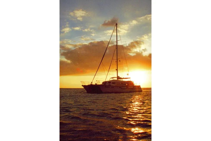 Liahona Yacht Photos Pics Sailboat silhouetted against a vibrant sunset, Custom 60 model, 1985.