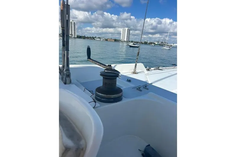 Liahona Yacht Photos Pics Sailboat deck view with winch, city skyline, and anchored boats under cloudy sky. Custom 60, 1985.