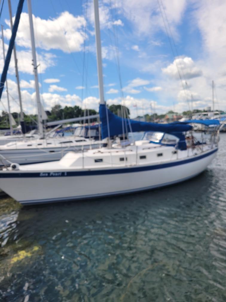 1985 Aloha 34 sailboat docked in a marina under a blue sky.
