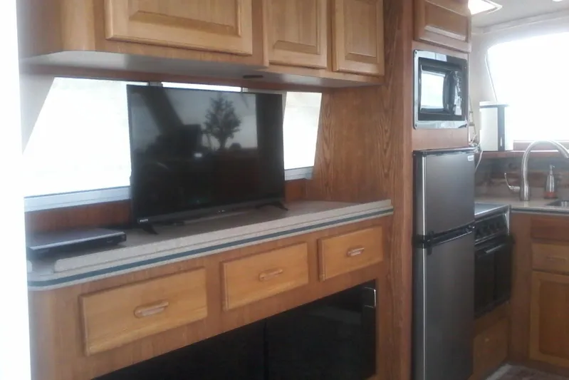 Lusea Yacht Photos Pics 1997 Mainship 350 interior with kitchen, TV, microwave, and wooden cabinetry.