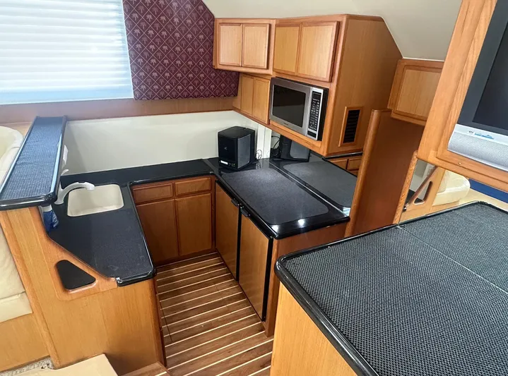 Current Addition Yacht Photos Pics 2006 Henriques 42 Convertible yacht kitchen with wood cabinetry, black countertops, and modern appliances.