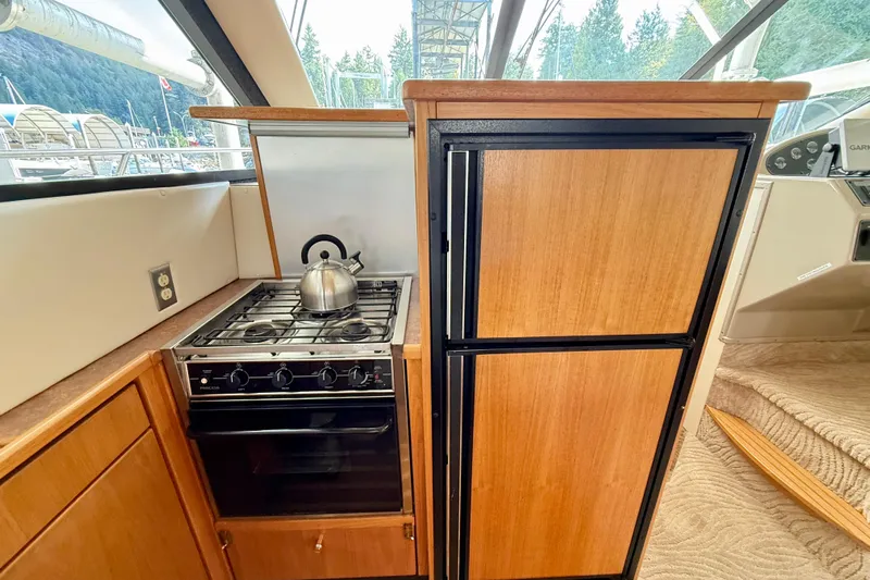 Pier Pressure Yacht Photos Pics 1999 Bayliner 3788 Command Bridge Motoryacht kitchen with stove, kettle, and wooden cabinetry.